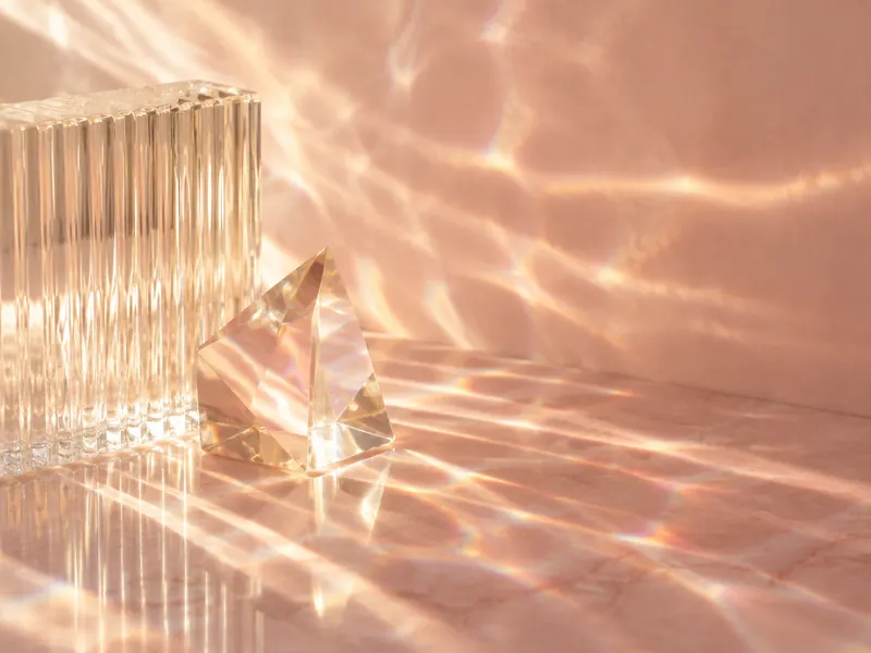 Sunlight passing through ribbed glass and a crystal prism, casting bands of warm light on blush stone